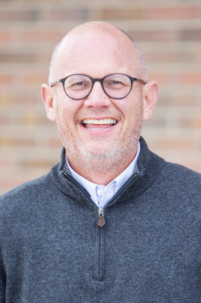 Stephen Loyd smiling while wearing a hoodie and glasses